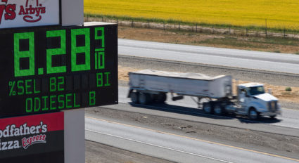 FILE PHOTO: Semis drive past sign showing fuel prices